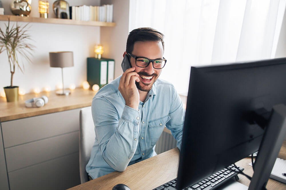 Smiling team member sitting at computer talking on phone during an IT support session