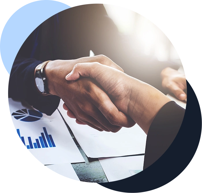 Color photo of two people shaking hands after a merger, with charts showing company data on it