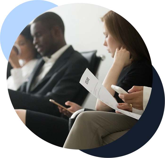 Color photograph of people in business attire sitting on chairs, holding their resumes and phones waiting to be interviewed